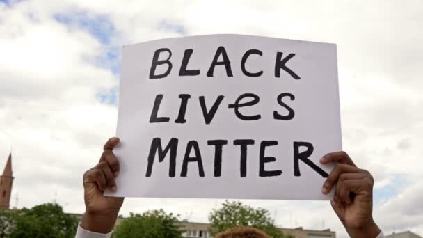 Zeichen BLACK LIVES MATTER in den Händen eines schwarzen Mannes. Gegen den Himmel. — Stockvideo
