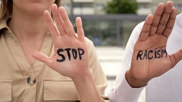 Stop RACISM skrivet på handflatorna av en vit tjej och en svart kille. Stoppa rasismen. — Stockvideo