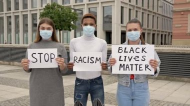 Farklı milletlerden üç genç ırk eşitsizliğini protesto ediyor. Ellerinde RACISM VE HAYATLARI DUR İÇİN posterleri var..