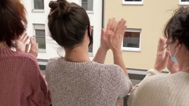 People rejoice at the end of the coronavirus epidemic. Three women in medical masks, standing on the balcony of an apartment building, cheerfully applaud. Rear view. — Stock Video