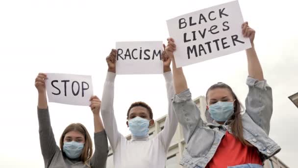医療マスクの3人の若者が人種の不平等に抗議している。彼らは彼らの手にポスターを持っています｜STOP RACISMとBLACK LIVE MATTER. — ストック動画