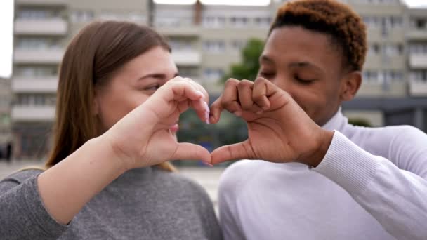 Kärlek mellan ung afrikansk man och vit kvinna. Ungdomar gör ett hjärttecken med sina egna händer. — Stockvideo