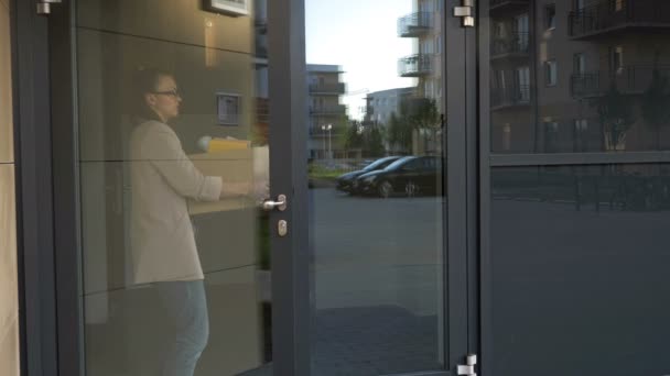 Una joven triste que acaba de perder su trabajo sale por la puerta de la oficina. En sus manos hay una caja con pertenencias personales. Crisis económica . — Vídeo de stock