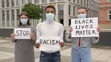 Farklı milletlerden üç genç ırk eşitsizliğini protesto ediyor. Ellerinde RACISM VE HAYATLARI DUR İÇİN posterleri var..