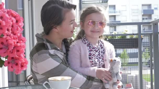 Die junge Frau sitzt mit ihrer sechsjährigen Tochter auf dem Balkon. Mama und Papa machen viel Spaß. Fotograf spiegelt sich in der Spiegelbrille des Mädchens. — Stockvideo