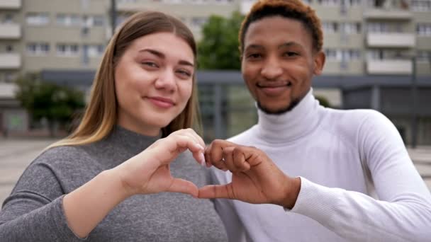 若いアフリカの男性と白人女性の間の愛。若い人たちは自分の手でハートサインをする. — ストック動画