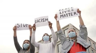 Tıbbi maskeli üç genç ırk eşitsizliğini protesto ediyor. Ellerinde RACISM VE HAYATLARI DUR İÇİN posterleri var..