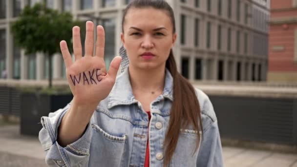 Um único manifestante. Jovem mulher séria mostra suas palmas em que está escrito Wake Up. Ela apela à acção . — Vídeo de Stock