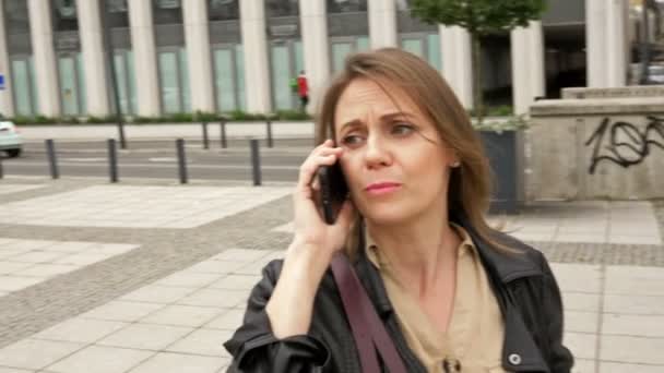 中年の女性が興奮して電話で誰かと話している。大都市の建物を背景に. — ストック動画