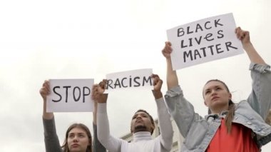 Farklı milletlerden üç genç ırk eşitsizliğini protesto ediyor. Ellerinde RACISM VE HAYATLARI DUR İÇİN posterleri var..