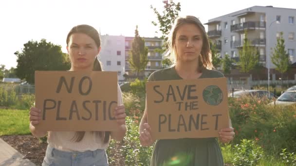 Duas jovens mulheres estão de pé com os cartazes SALVAR O PLANETA e NÃO PLÁSTICO. Dão um contributo viável para a luta contra a poluição global da natureza . — Vídeo de Stock