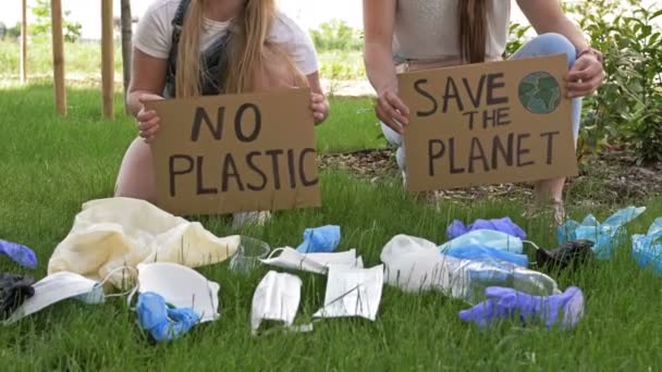 Dvě mladé ženy dřepící u hromady odpadků s plakáty BEZPEČÍ PLANET a ŽÁDNÉ PLASTY. Během pandemie COVID-19 byly přidány tuny odpadků. — Stock video