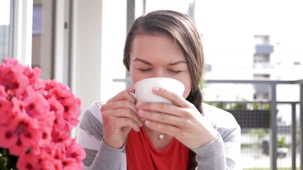 Портрет симпатичной брюнетки с чашкой утреннего кофе. Женщина сидит на балконе и счастливо улыбается. . — стоковое видео