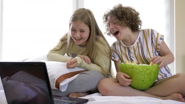 Retrato de adolescentes felices viendo comedia en la cama y riendo. Amigos alegres comiendo palomitas de maíz sabrosas y mirando la película con alegría. — Vídeos de Stock