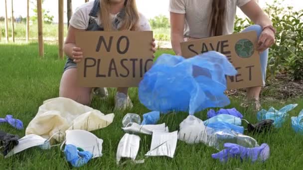 Dvě mladé ženy dřepící u hromady odpadků s plakáty BEZPEČÍ PLANET a ŽÁDNÉ PLASTY. Během pandemie COVID-19 byly přidány tuny odpadků. — Stock video