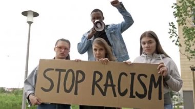 Bir grup gencin elinde bir RACISM posteri var. Koyu tenli genç protestocu megafona slogan attı.