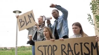 Bir grup gencin elinde STOP RACISM ve BLM posterleri var. Koyu tenli genç protestocu megafona slogan attı.