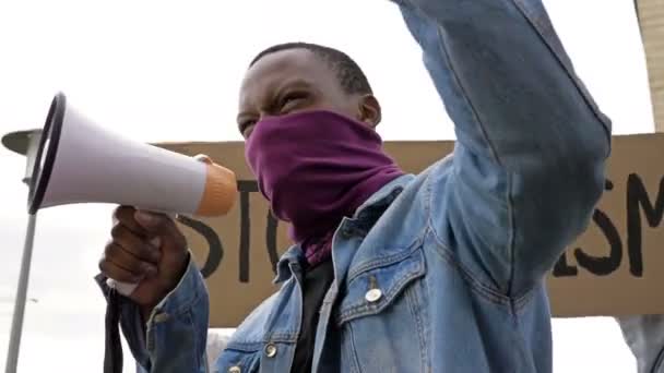 Bei einem Protest gegen Rassismus schreit dunkelhäutiger junger Demonstrant wütend in Megafon. — Stockvideo