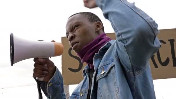 En una protesta contra el racismo, un joven manifestante de piel oscura grita furioso en megáfono . — Vídeo de stock