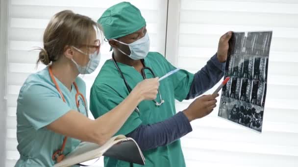 Två läkare undersöker röntgenbilder av patienten för diagnos. Begreppet avsaknad av motsägelser mellan raser i ett team av yrkesutövare. — Stockvideo