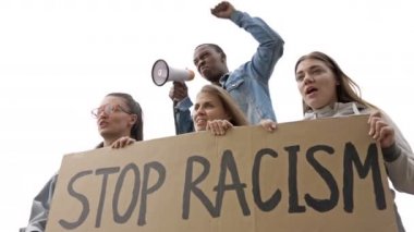Bir grup gencin elinde bir RACISM posteri var. Koyu tenli genç protestocu megafona slogan attı.