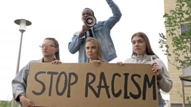 Bir grup gencin elinde bir RACISM posteri var. Koyu tenli genç protestocu megafona slogan attı. BLM.