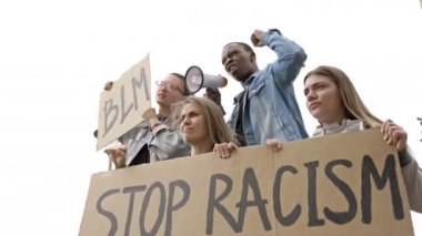 Bir grup gencin elinde STOP RACISM ve BLM posterleri var. Koyu tenli genç protestocu megafona slogan attı.