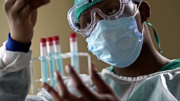 Jovem assistente de laboratório de pele escura analisando uma amostra de sangue em um tubo de teste em um laboratório . — Vídeo de Stock