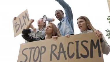 Bir grup gencin elinde STOP RACISM ve BLM posterleri var. Koyu tenli genç protestocu megafona slogan attı.