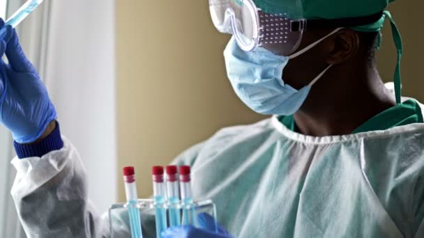 Jeune assistant de laboratoire à la peau foncée analysant un échantillon de sang dans un tube à essai dans un laboratoire. — Video