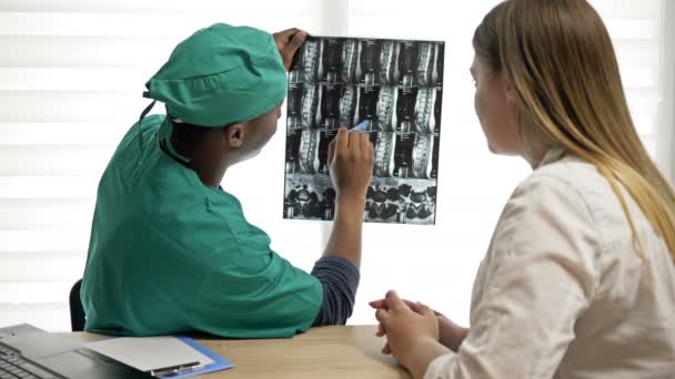 Afrikaanse mannelijke traumatoloog legt röntgenfoto 's uit aan de patiënt. — Stockvideo