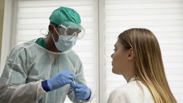 Un joven médico africano toma una muestra de garganta de una paciente femenina. Prueba del coronovirus, prueba para determinar la infección por coronovirus . — Vídeo de stock