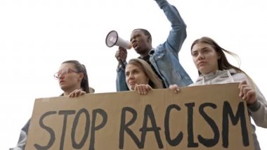 Bir grup gencin elinde bir RACISM posteri var. Koyu tenli genç protestocu megafona slogan attı. BLM.