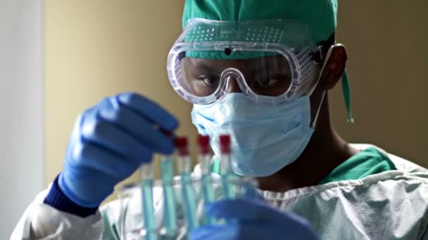 Ung mörkhyad manlig labbassistent som analyserar ett blodprov i ett provrör i ett laboratorium. — Stockvideo