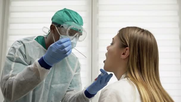 Un joven médico africano toma una muestra de garganta de una paciente femenina. Prueba del coronovirus, prueba para determinar la infección por coronovirus . — Vídeo de stock