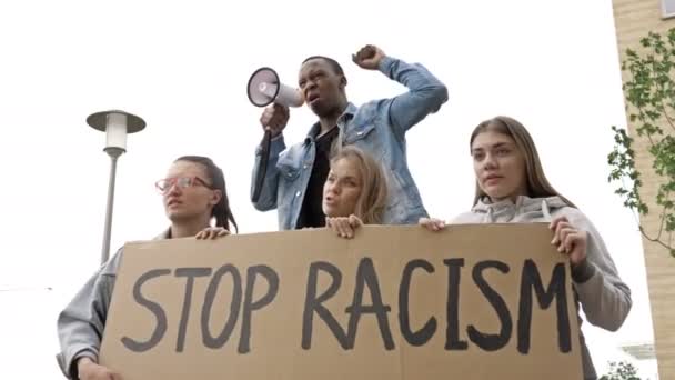 Le persone multietniche che protestano per la parità dei diritti tengono manifesto Stop al razzismo. Il giovane protestante dalla pelle scura grida slogan in un megafono. — Video Stock