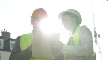 İki müteahhit, bir adam ve genç bir kadın inşaat alanında bir şey tartışıyorlar..