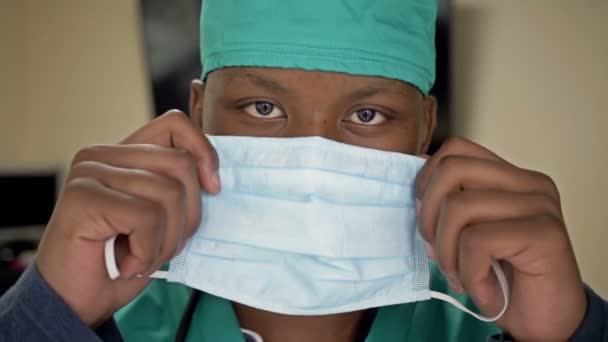 Jovem médico negro ou estagiário coloca uma máscara médica enquanto se prepara para o trabalho . — Vídeo de Stock