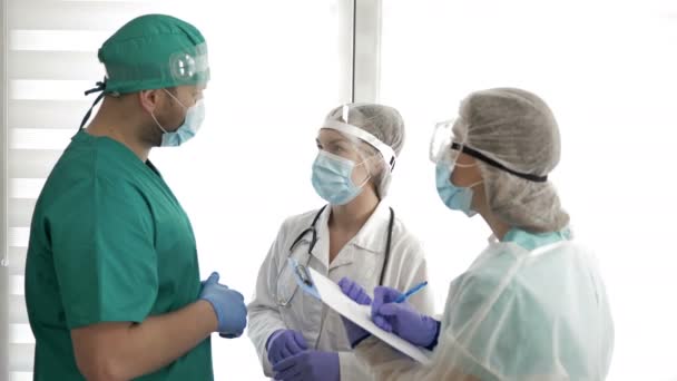 Two doctors in protective uniforms are discussing something and giving directions to the nurse. Covid-19. — Stock Video