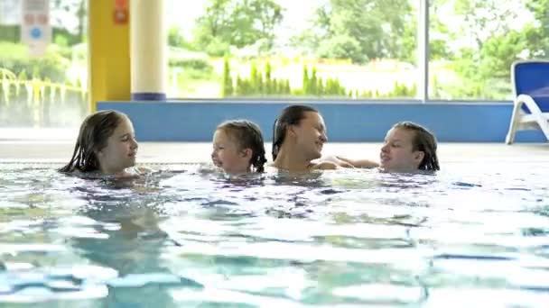 Vacaciones familiares en la piscina. Una mujer joven y tres chicas se divierten nadando en la piscina . — Vídeos de Stock