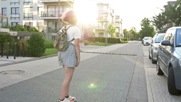 Su uno skateboard a scuola. Ragazza adolescente con uno zaino in una strada della città. Ritorno a scuola. — Video Stock