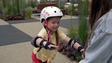 Anne küçük kızına paten kaymayı öğretiyor. Genç kadın kızların elini tutuyor..