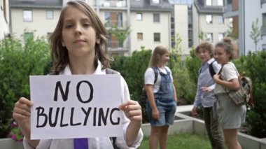 Zorbalığa hayır posterli bir okul çocuğunun portresi. Gülen sınıf arkadaşlarının arka planına karşı. Çocuk zulmü.