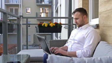Serbest ve uzaktan kumandalı. İş adamı evde balkonda otururken dizüstü bilgisayarda çalışıyor..