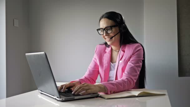 Aantrekkelijke vrouw werkt aan de computer in het kantoor. Ze communiceert vriendelijk met de klant en schrijft iets op.. — Stockvideo