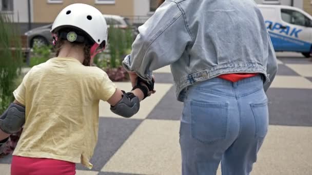 Mom teaches little daughter to roller skate. The woman holds the child by the hand. Back view. — Stock Video