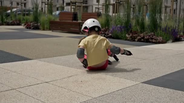 Kleines Mädchen stürzt beim Rollschuhlaufen. Sie kommt kaum auf die Beine, um weiter Schlittschuh zu laufen. Das Kind lächelt. — Stockvideo