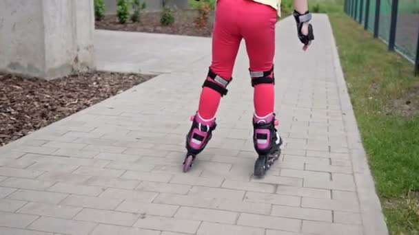 Uma menina de 5-6 anos está patinando no pátio de um prédio de apartamentos. A criança está apenas começando a dominar patins, então ele muitas vezes cai . — Vídeo de Stock