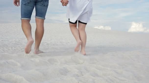 Dois amantes caminham ao longo da areia branca de mãos dadas. Contra o fundo do céu em nuvens brancas. Visão traseira . — Vídeo de Stock