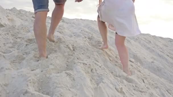 A szerelmesek kéz a kézben másznak fel egy homokos dombra.. — Stock videók